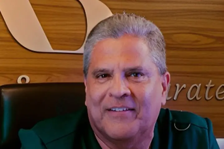 Retrato del Dr. Alberto Saravia Zárate sonriendo frente a un panel de madera en su consultorio.